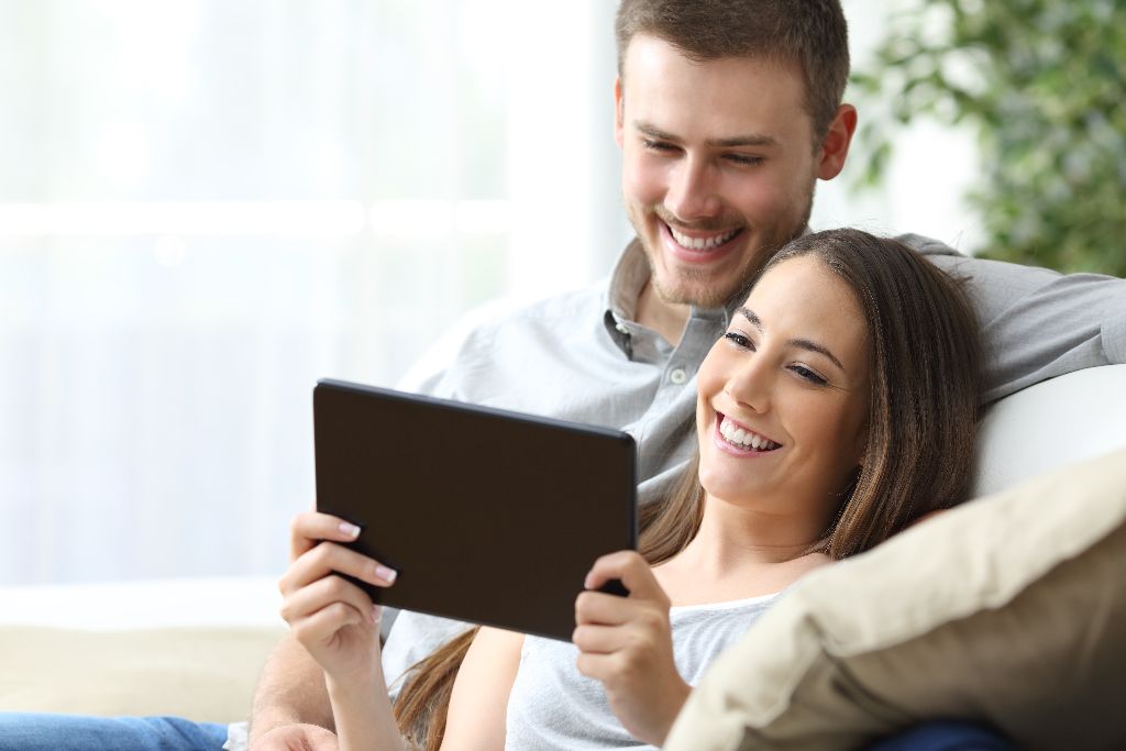 Casual couple watching media content on line in a tablet sitting on a sofa in the living room at home
